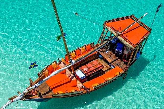 A traditional dhow with orange cushions anchored on clear turquoise water off Zanzibar.