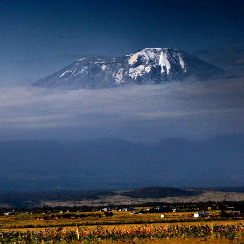A trekker approaching the snow-capped summit of Mount Kenya at dawn.